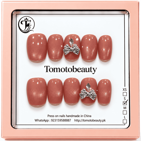 Tomoto Beauty B023: Warm peach-coral glossy nails with refined fine shimmer and a shiny silver rhinestone bow feature. A romantic short square design.