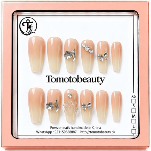 Tomoto Beauty C103 – Peach Nude Ombré Silver Bow Press On Nails. Soft peach-to-cream ombré nails with silver butterfly and ribbon bow charms, and small sparkling crystals.