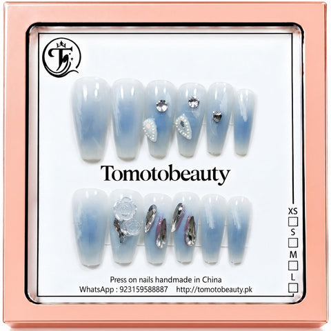 Tomoto Beauty C105 – Icy Blue Ombré Crystal Press On Nails. Icy blue and translucent white ombré coffin-style nails with sparkling clear stones, silver metallic accents and translucent floral charms.